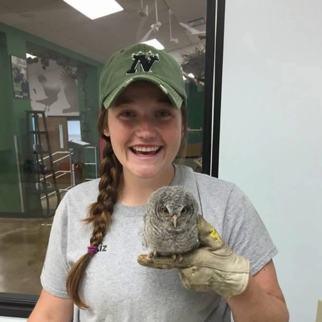 Woman in green cap holding a small owl on gloved hand