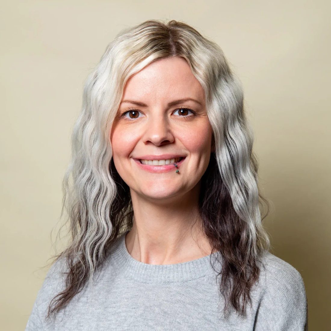 Woman with wavy gray hair in gray sweater smiling